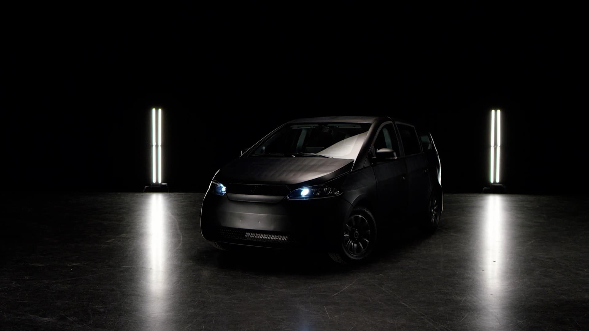 Das schwarze Elektro Auto Sion von Sono Motors vor einem ausdrucksvollen schwarzen Hintergrund.