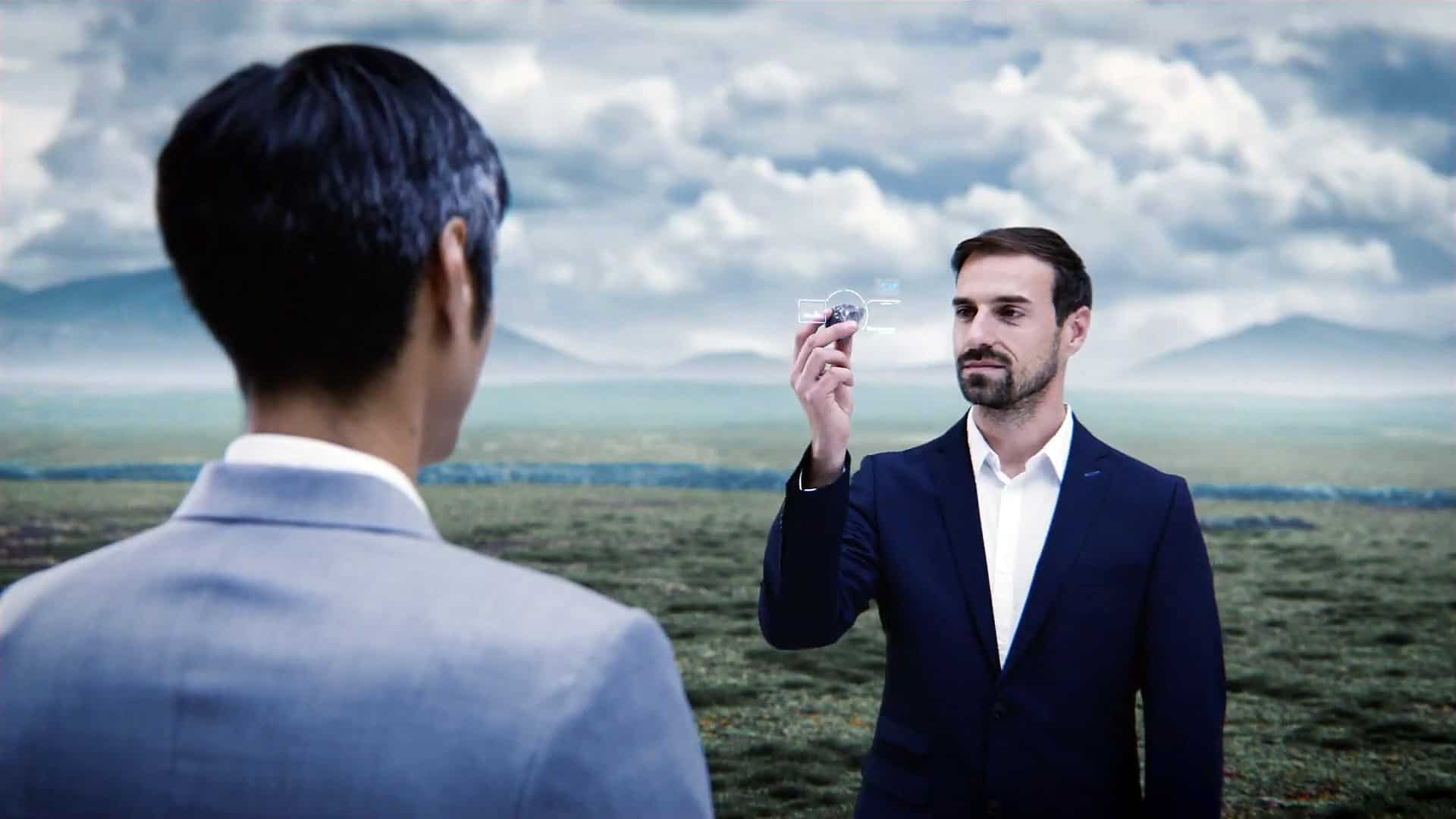 Der Anzug tragende Dürr Mitarbeiter hält dem Kunden auf einer Landschaft einen Stein vor, der von einem virtuellen Schema umkreist ist.