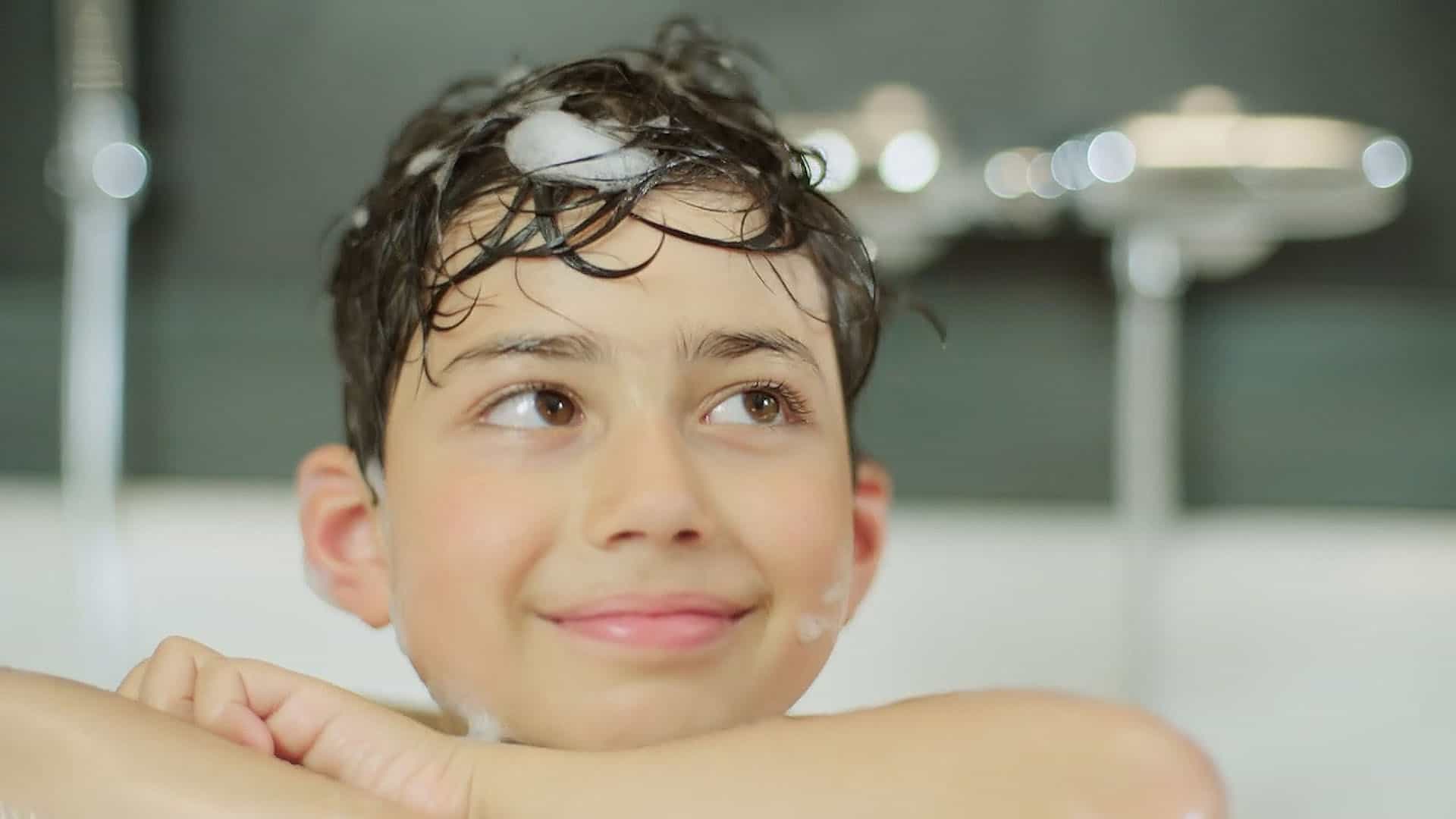 Ein glückliches Kind in der Badewanne mit shampoonierten Haare.